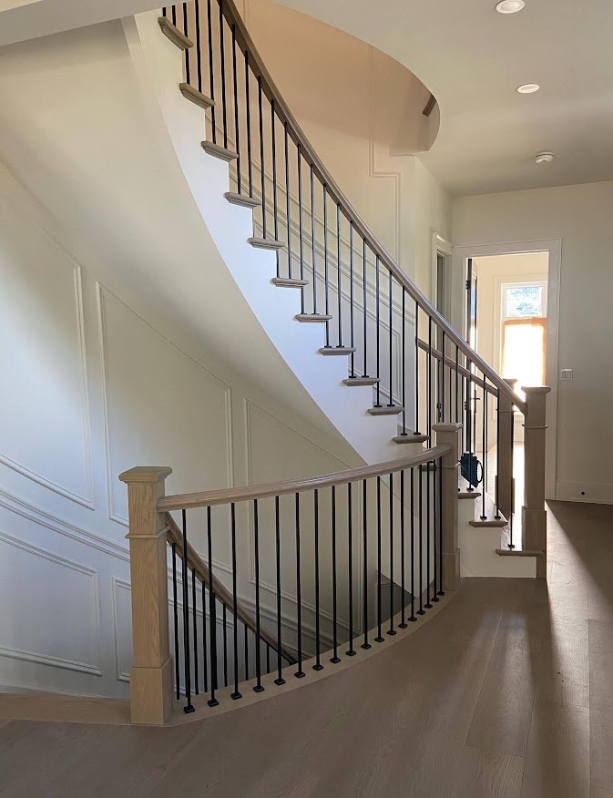 A double staircase in an entry that is curving with white walls and brand new hardwood floors.