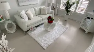 A professional vinyl wood flooring installation done in a living room with a white rug, white sofa, and glass top tables.